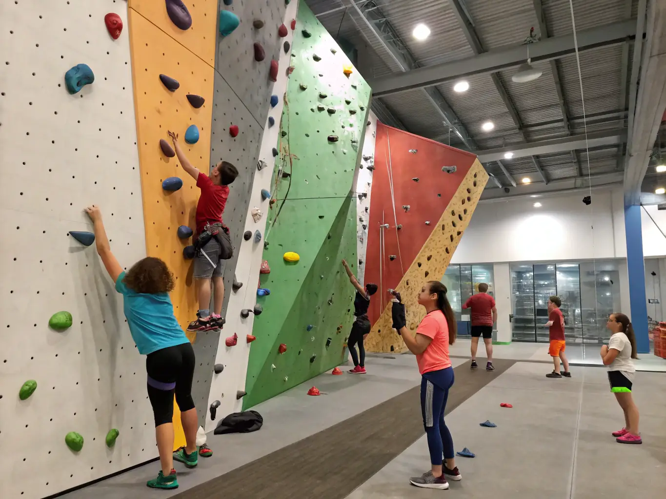 A dynamic shot of climbers of various ages and skill levels scaling an indoor climbing wall, showcasing the inclusive and supportive environment of AURILLAC MONTAGNE ESCALADE.